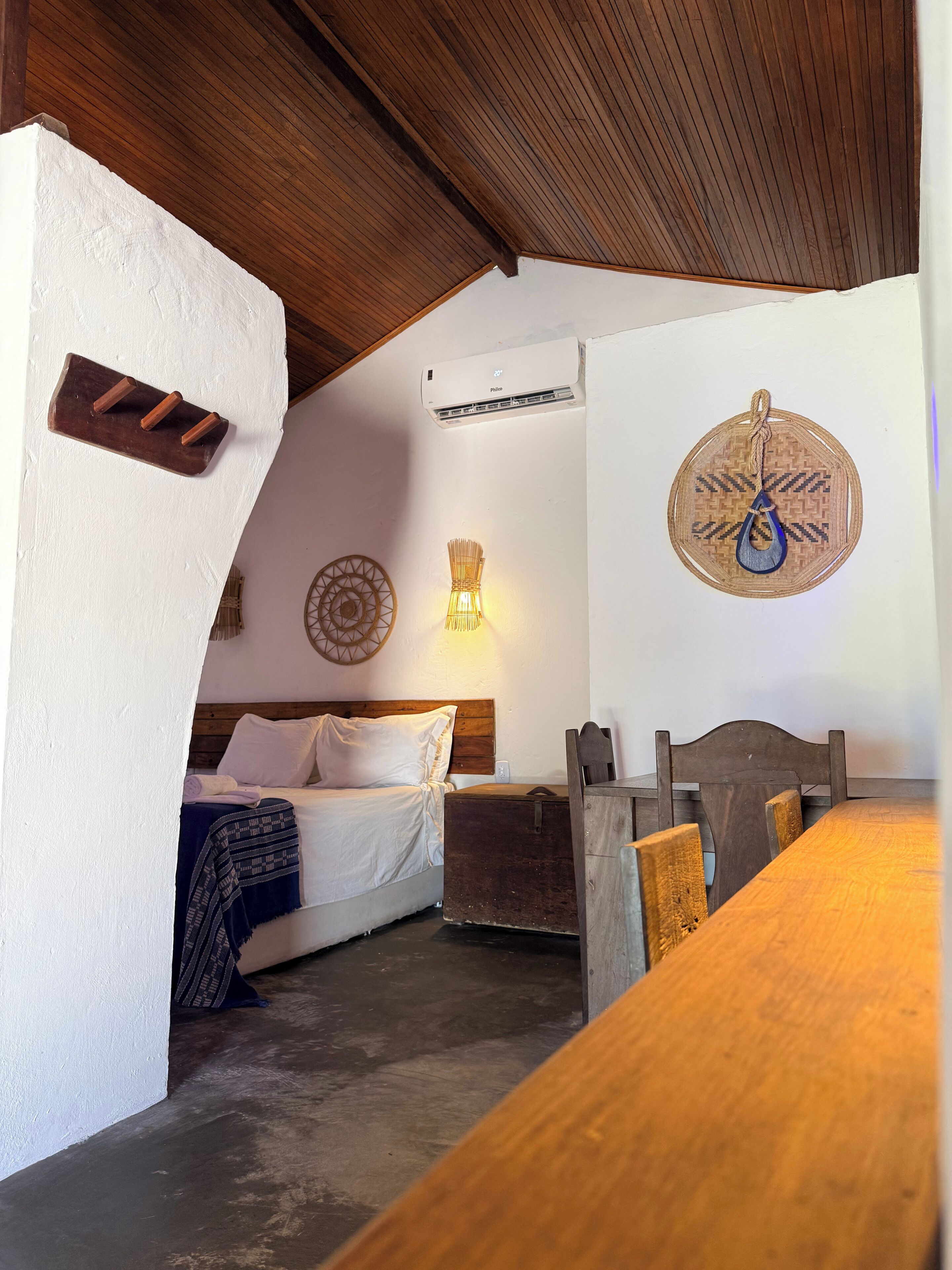 Una habitación con cama, una mesa, aire acondicionado de pared y un adorno en la pared.
