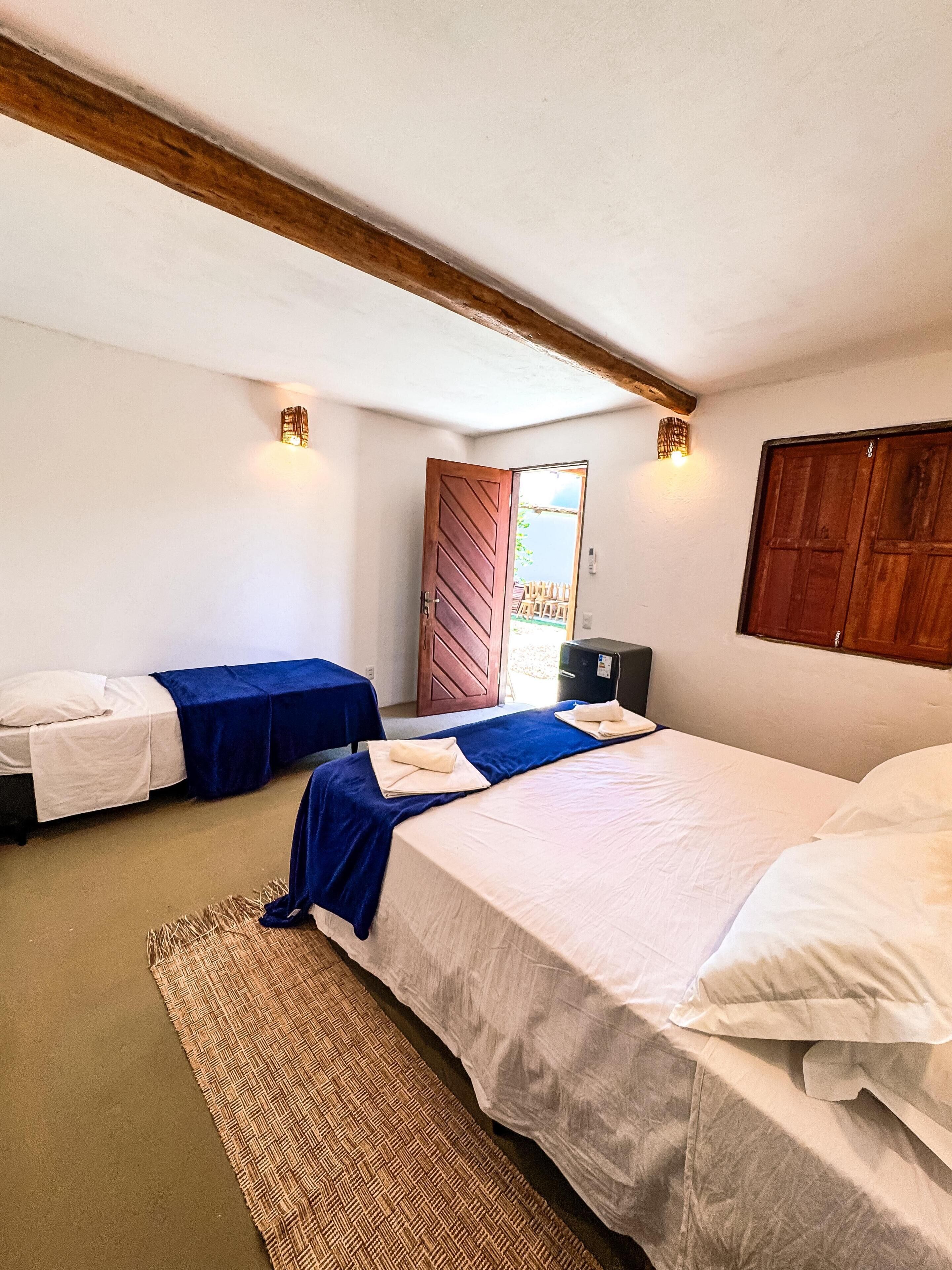 A room with two beds, a desk, a chair, a small table, and a door leading outside.