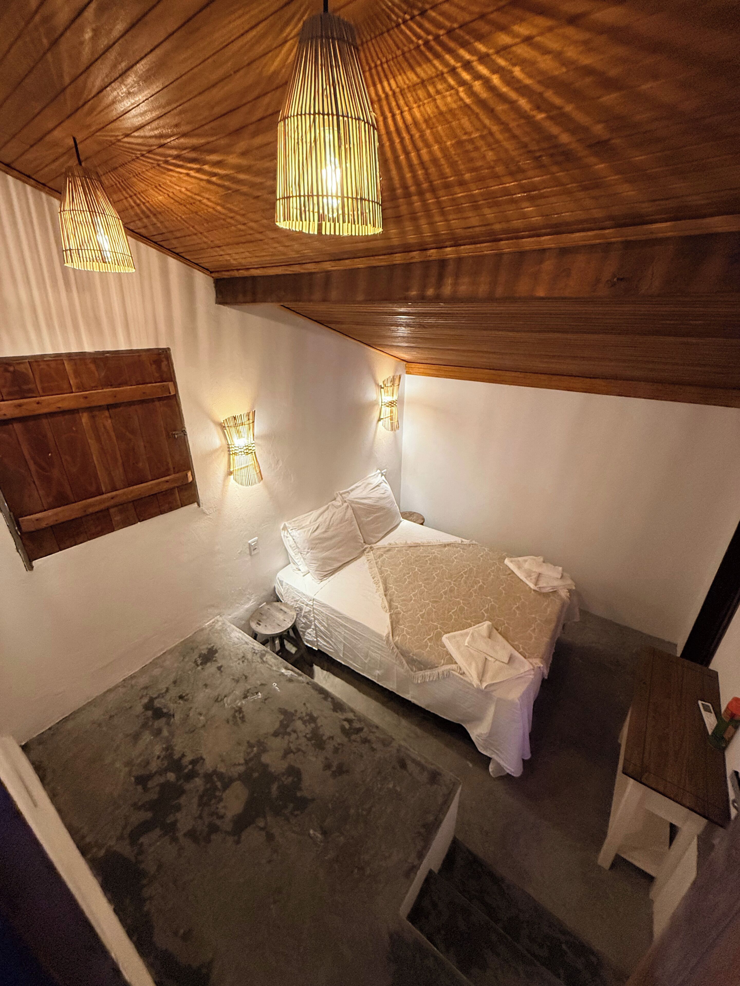 Une pièce comprenant un lit, une petite table, un tabouret et deux lampes fixées au mur.