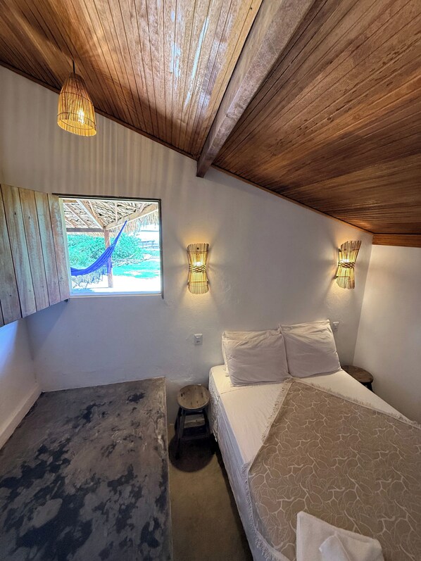 A bedroom with a bed, two wall-mounted lamps, a window with a view, and a hammock outside. - Atins Beach House (Barreirinhas)