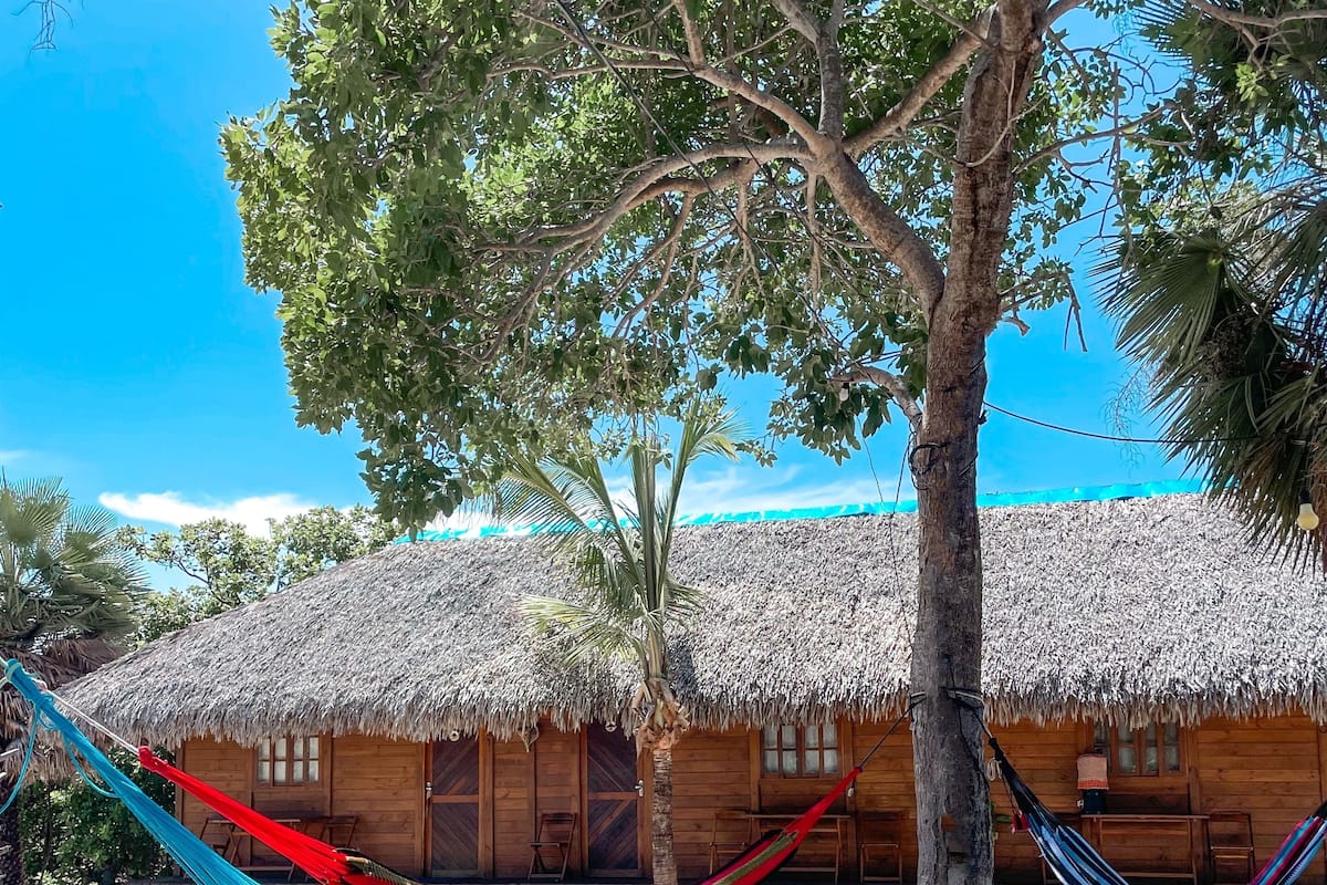 A thatched-roof hut with a hammock and wooden furniture in a sunny outdoor setting.