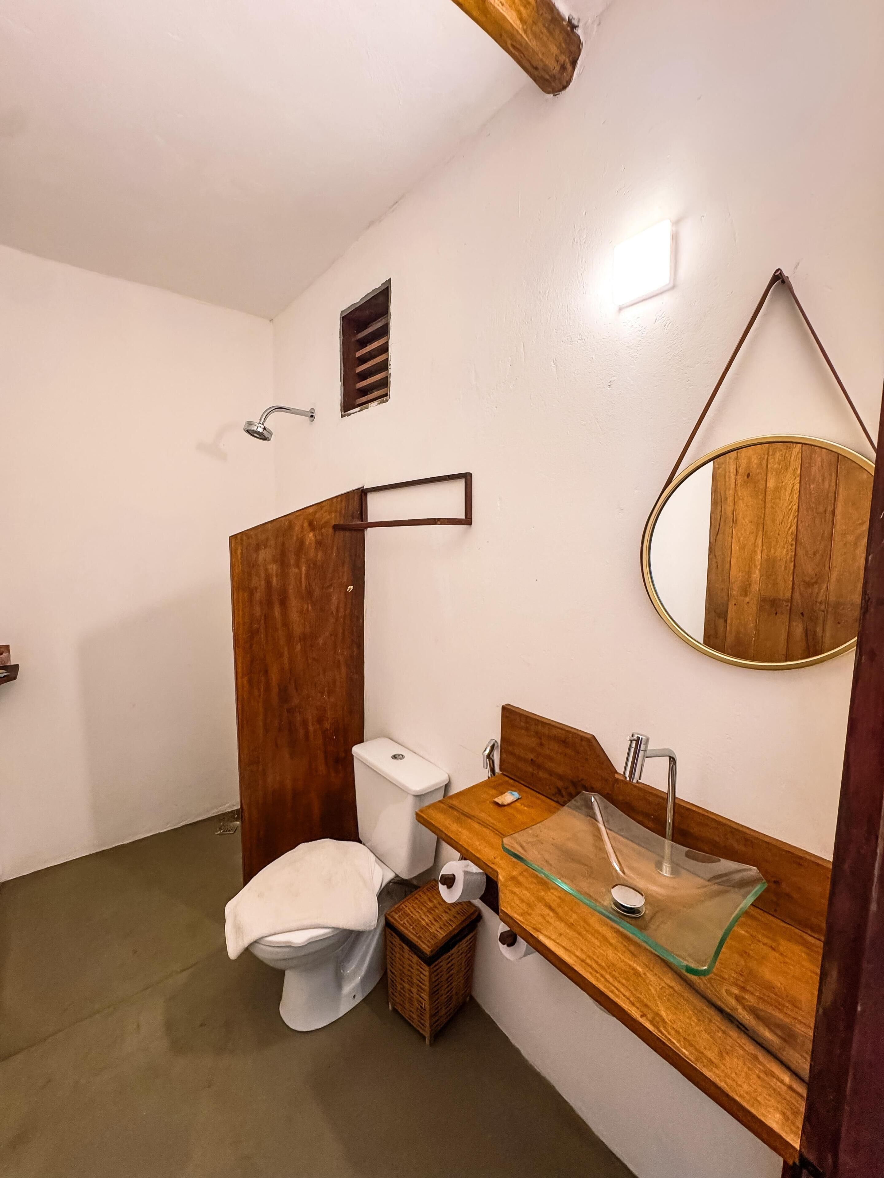Un baño con tocador de madera, lavamanos de vidrio, inodoro y ducha.