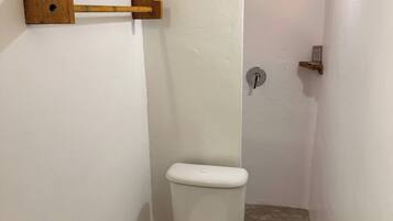 A small, narrow bathroom with a white toilet, a wooden towel rack, a metal faucet, and a light fixture.
