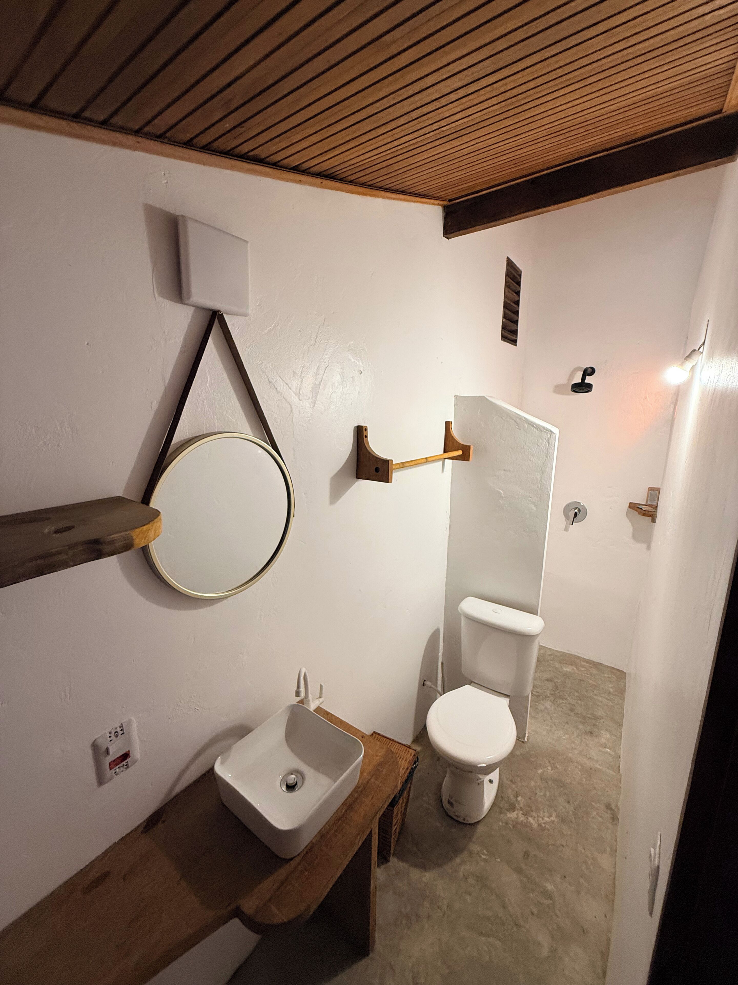 A bathroom with a wooden vanity, a round mirror, a toilet, and a wall-mounted towel rack.