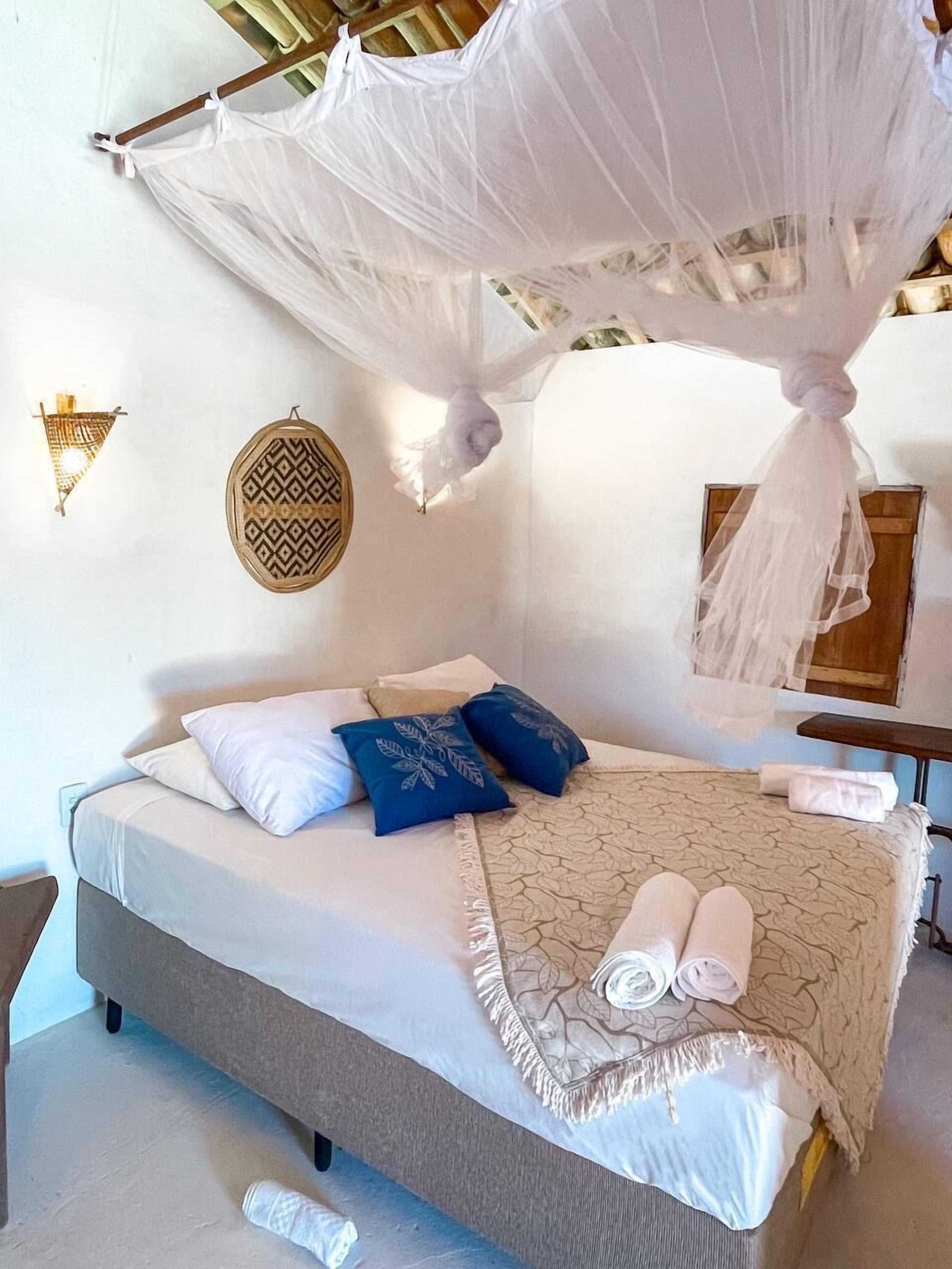A neatly made bed with a canopy, pillows, and rolled towels.