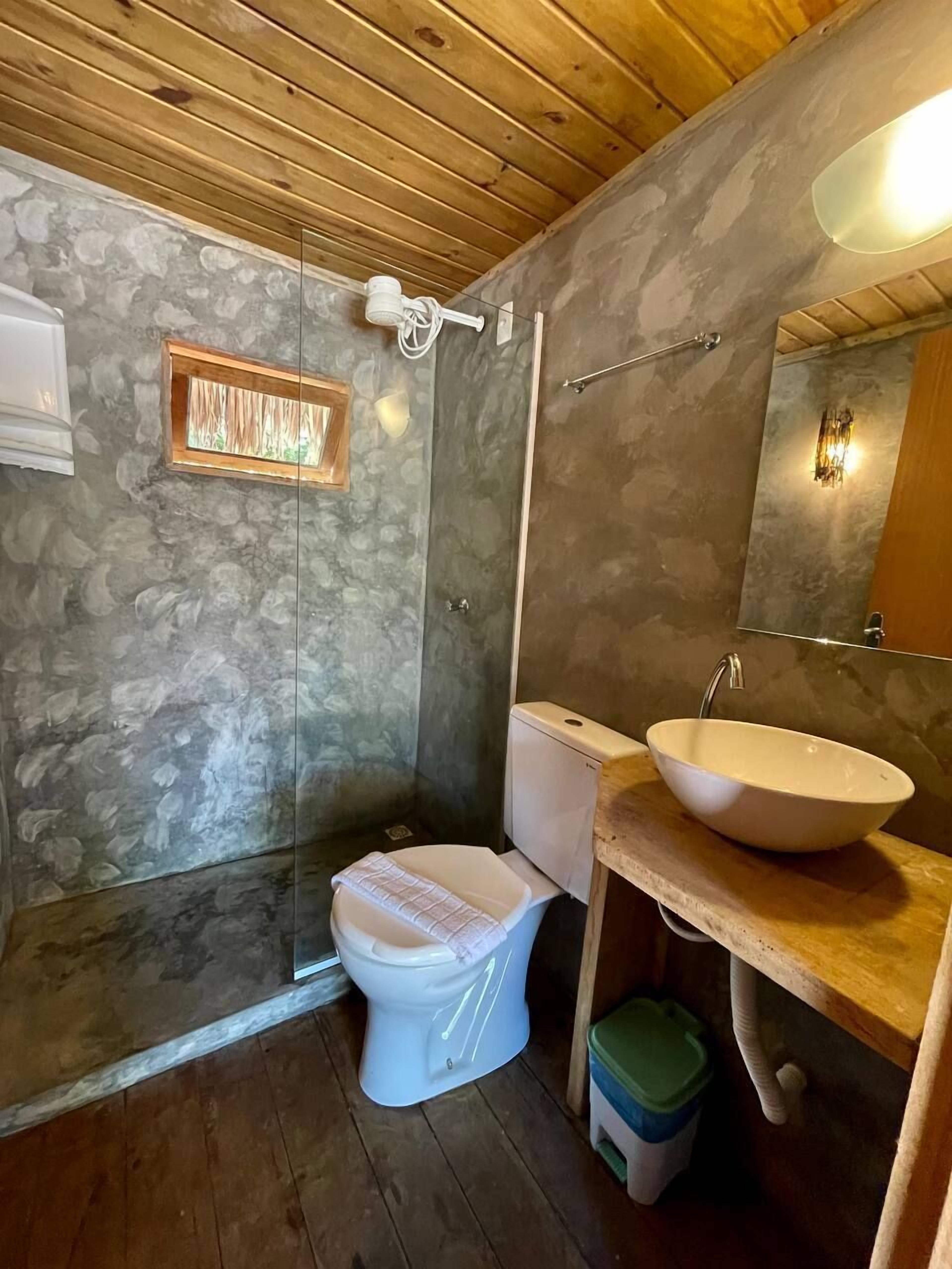 A bathroom with a stone wall, a wooden ceiling, a white toilet, a wooden sink, and a glass shower enclosure.