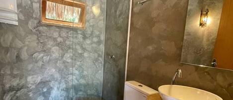 A bathroom with a stone wall, a wooden ceiling, a white toilet, a wooden sink, and a glass shower enclosure.
