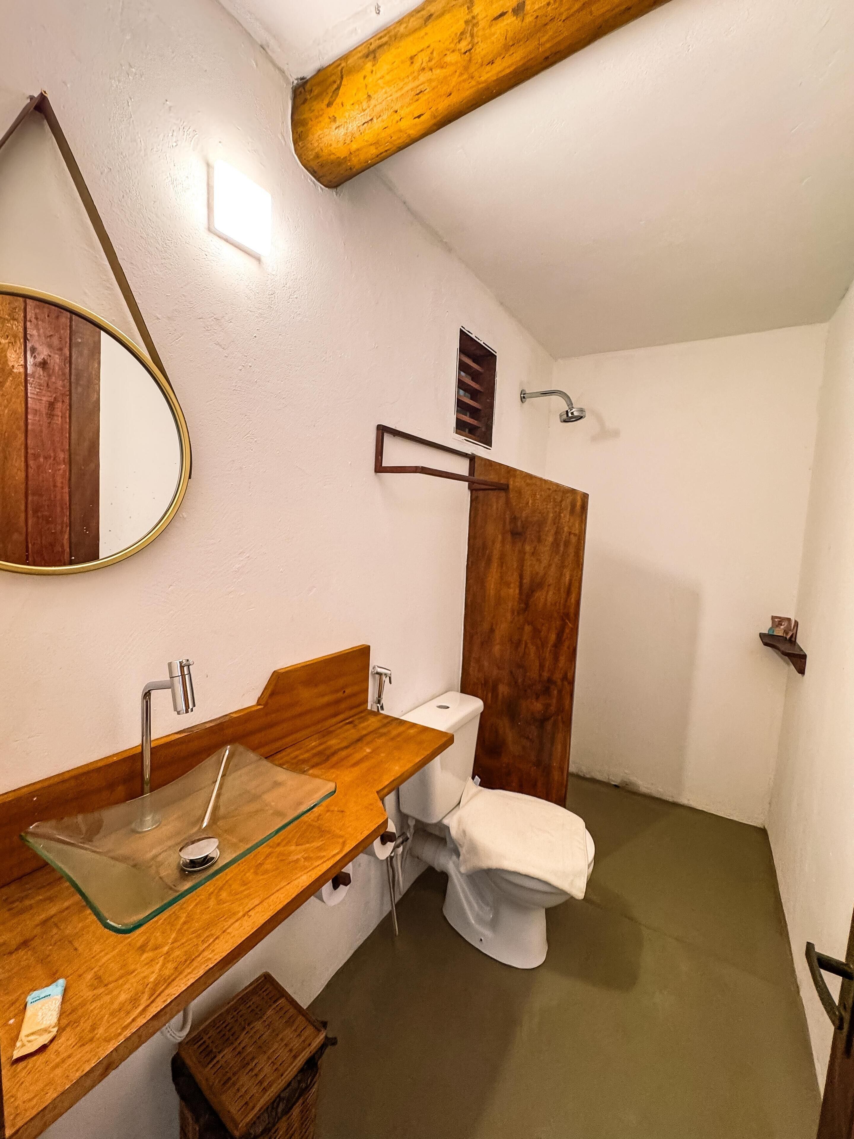 Une salle de bain avec un meuble-lavabo en bois, un lavabo en verre, des toilettes blanches et un espace douche.
