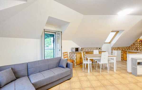 A modern apartment with a grey sofa, a dining area with white chairs, and a kitchen with a tiled backsplash.