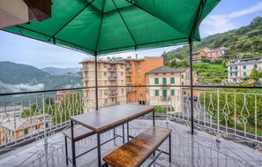 A terrace with a table and bench, overlooking a hillside with buildings.