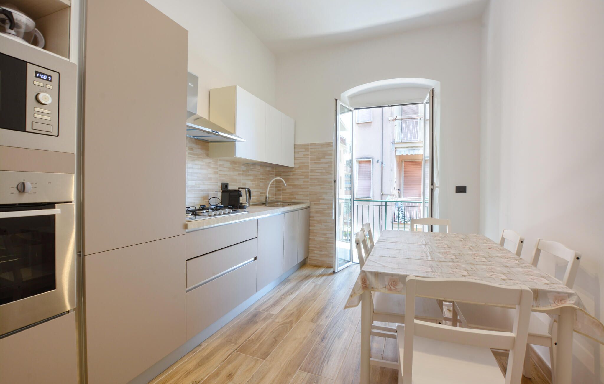 Eine kompakte Küche mit modernen Geräten, ein Essbereich mit Tisch und Stühlen und ein Blick auf einen Balkon.