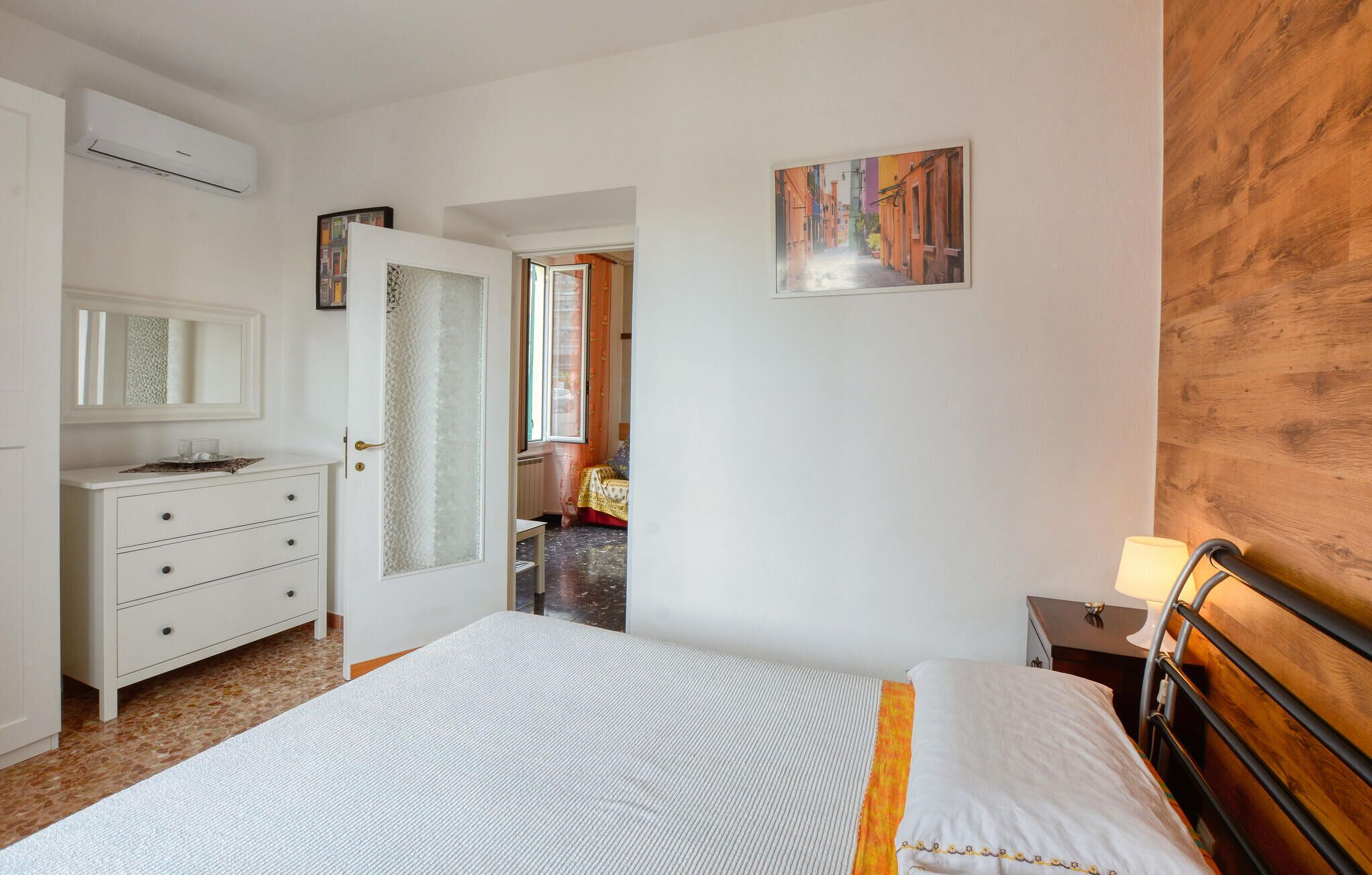 Une chambre à coucher comprenant un lit, une commode, une table de chevet, un tableau et une porte donnant sur une autre pièce.