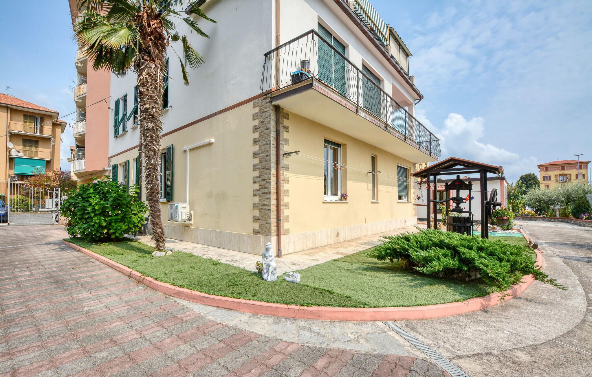A two-story residential building with a balcony, a small garden area with a palm tree, and a water feature.