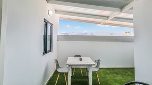Pequeña habitación con una mesa, dos sillas, ventanal con vistas a montañas y suelo de césped artificial.