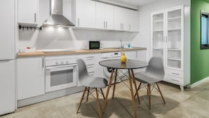 Una cocina moderna con armarios blancos, un microondas, una estufa y un comedor con dos sillas y una mesa.