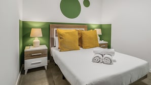 Un dormitorio ordenado con cama, dos mesitas de noche, una lámpara y un detalle decorativo en la pared color verde.