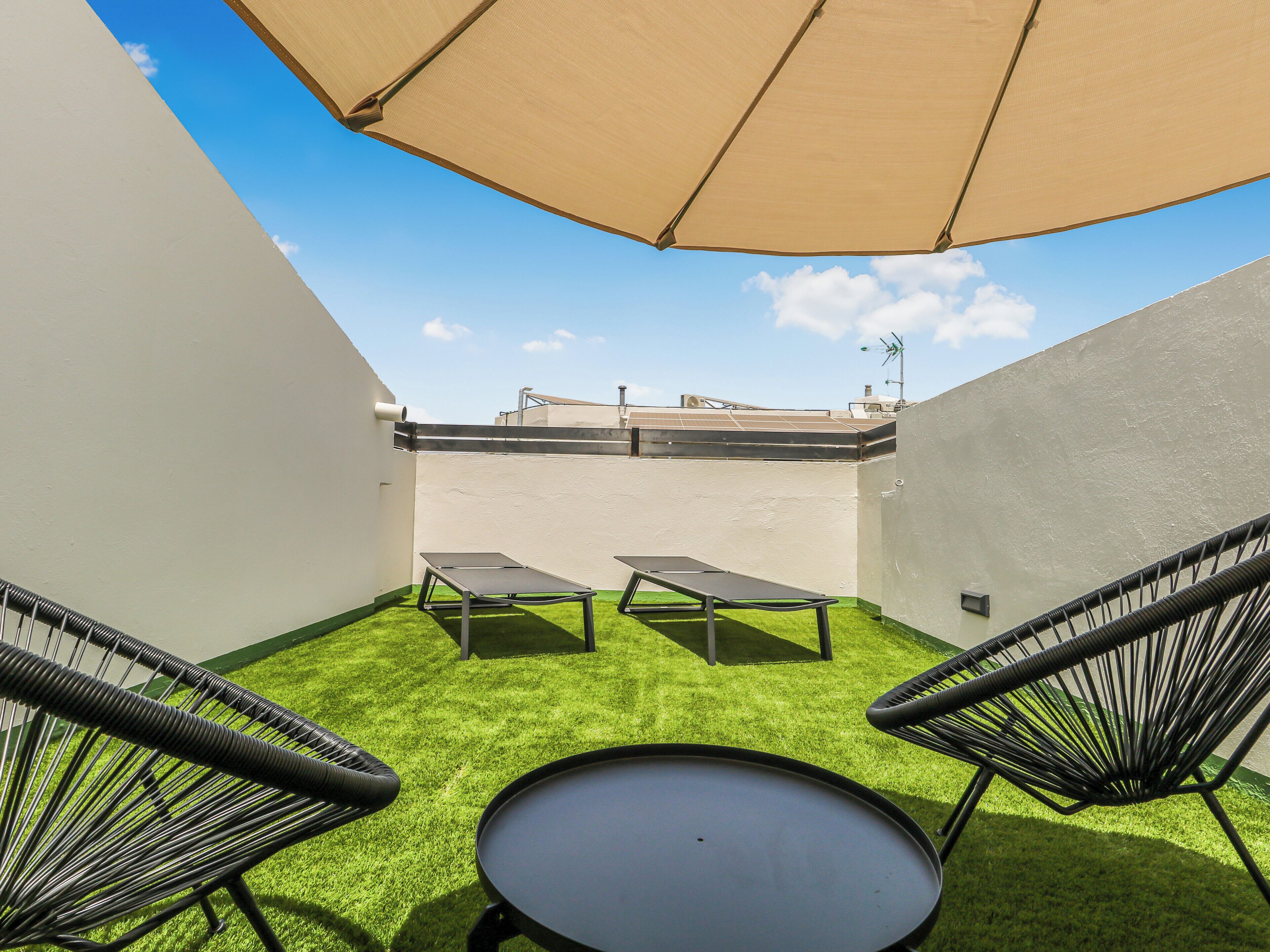 A rooftop patio with two lounge chairs, a small table, and a large umbrella providing shade.