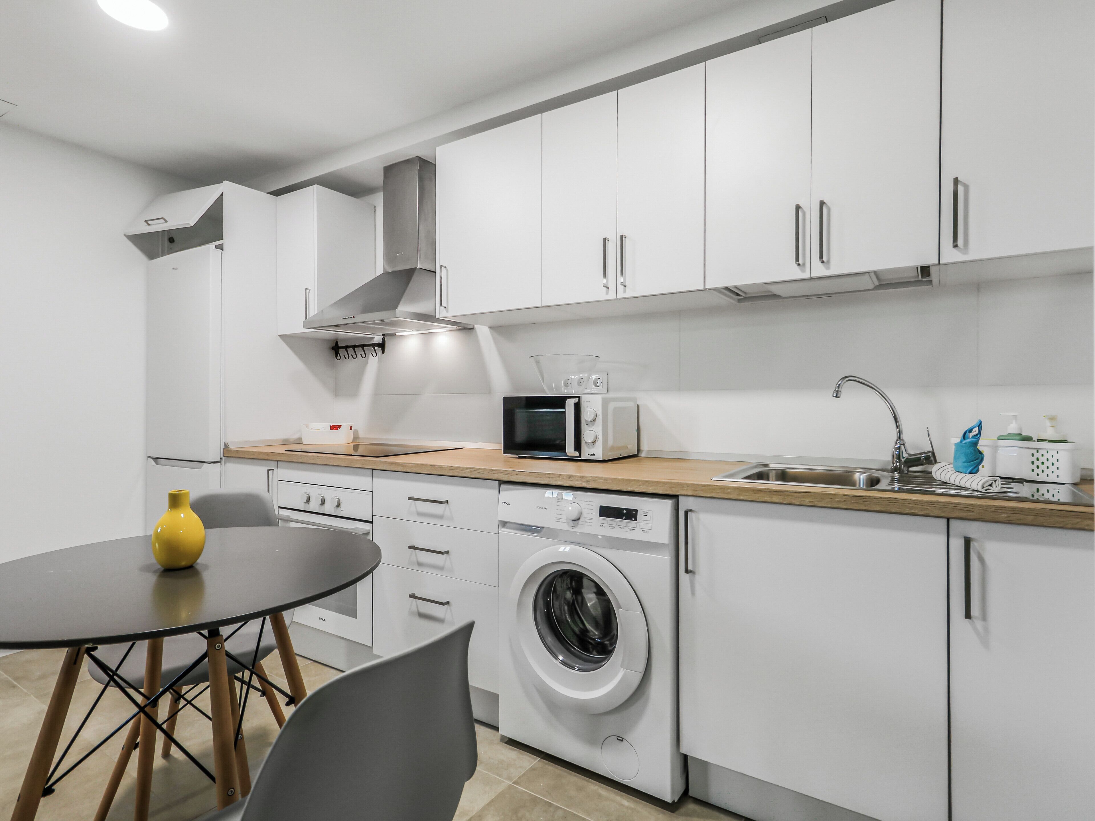 A modern kitchen with white cabinets, a microwave, a washing machine, and a sink.