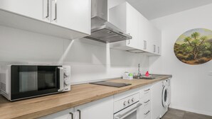 Une cuisine moderne avec des meubles blancs, un four à micro-ondes, une cuisinière et un lave-linge.