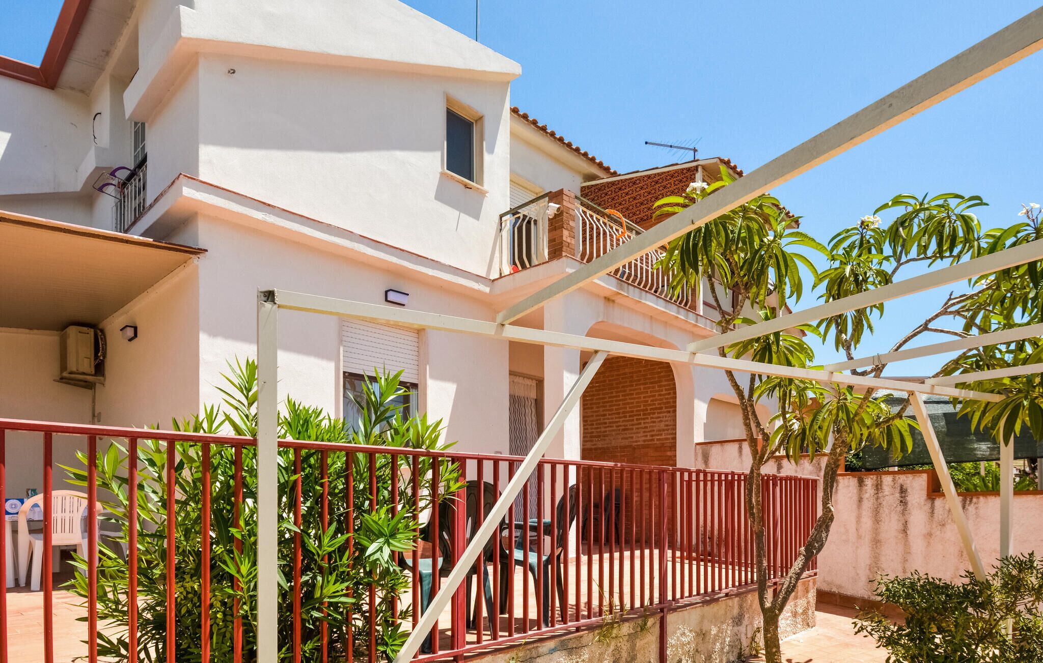 A two-story house with a balcony, a red metal fence, and potted plants.