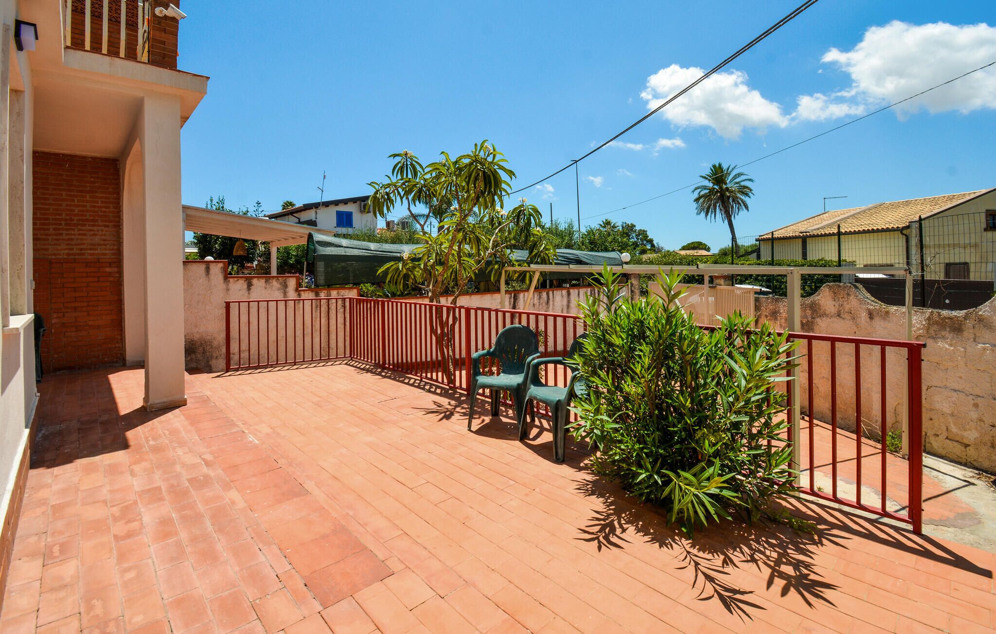 A patio with a red fence, green chairs, and potted plants.