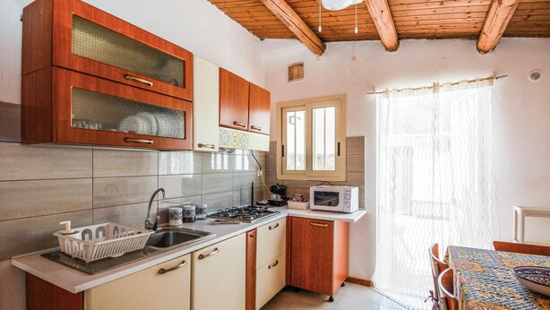 A kitchen with wooden cabinets, a microwave, a sink, and a window with curtains. - Lovely home in Marzamemi with WiFi (Marzamemi)