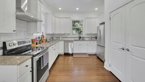 A modern kitchen with white cabinetry, stainless steel appliances, and a wooden floor. - Charming 3BR Retreat - Spacious Deck, Backyard (Atlanta)