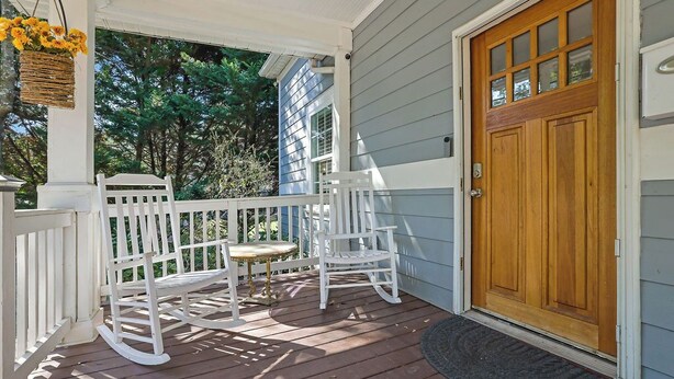 A porch with white rocking chairs and a small table, a wooden door, and a basket of flowers. - Charming 3BR Retreat - Spacious Deck, Backyard (Atlanta)