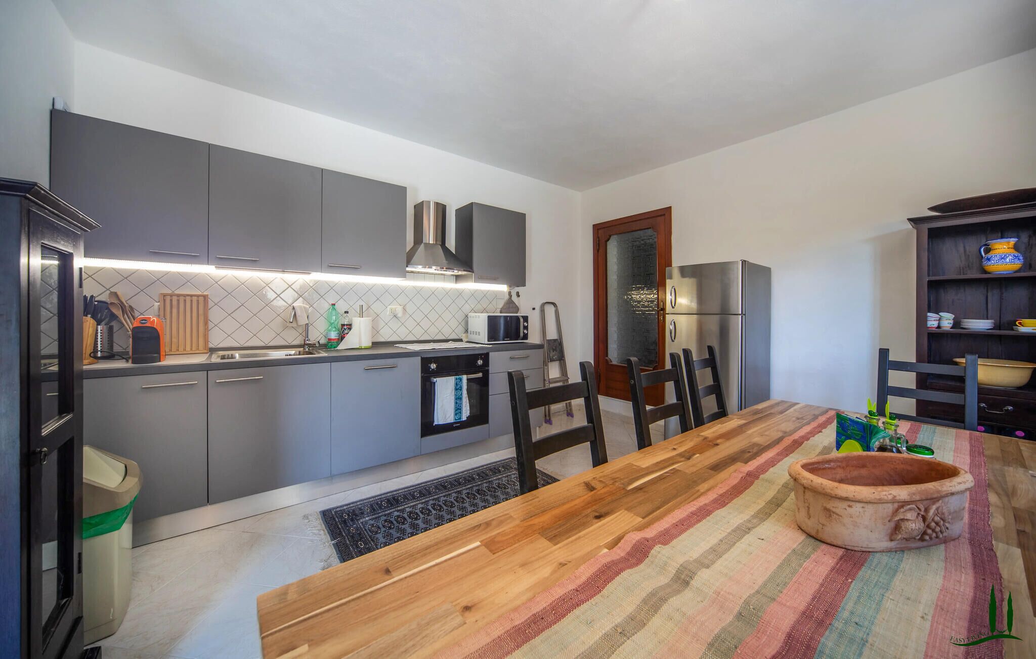 A compact kitchen with grey cabinets, a microwave, a refrigerator, and a dining table with chairs.