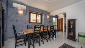 Un coin repas avec une longue table et des chaises en bois, un appareil de climatisation et un meuble contenant un bol rouge.
