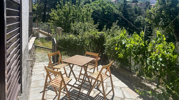 Une terrasse extérieure avec un sol en pierre, une table et des chaises en bois, et une vue sur un vignoble.