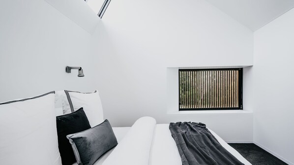 A minimalist bedroom with a bed, a window with vertical blinds, and a wall-mounted light fixture.