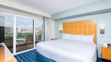 A hotel room with a large bed, a television, a balcony with a table and chairs, and a city view.