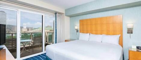 Habitación de hotel con una cama grande, televisión, balcón con mesa y sillas, y vistas a la ciudad.