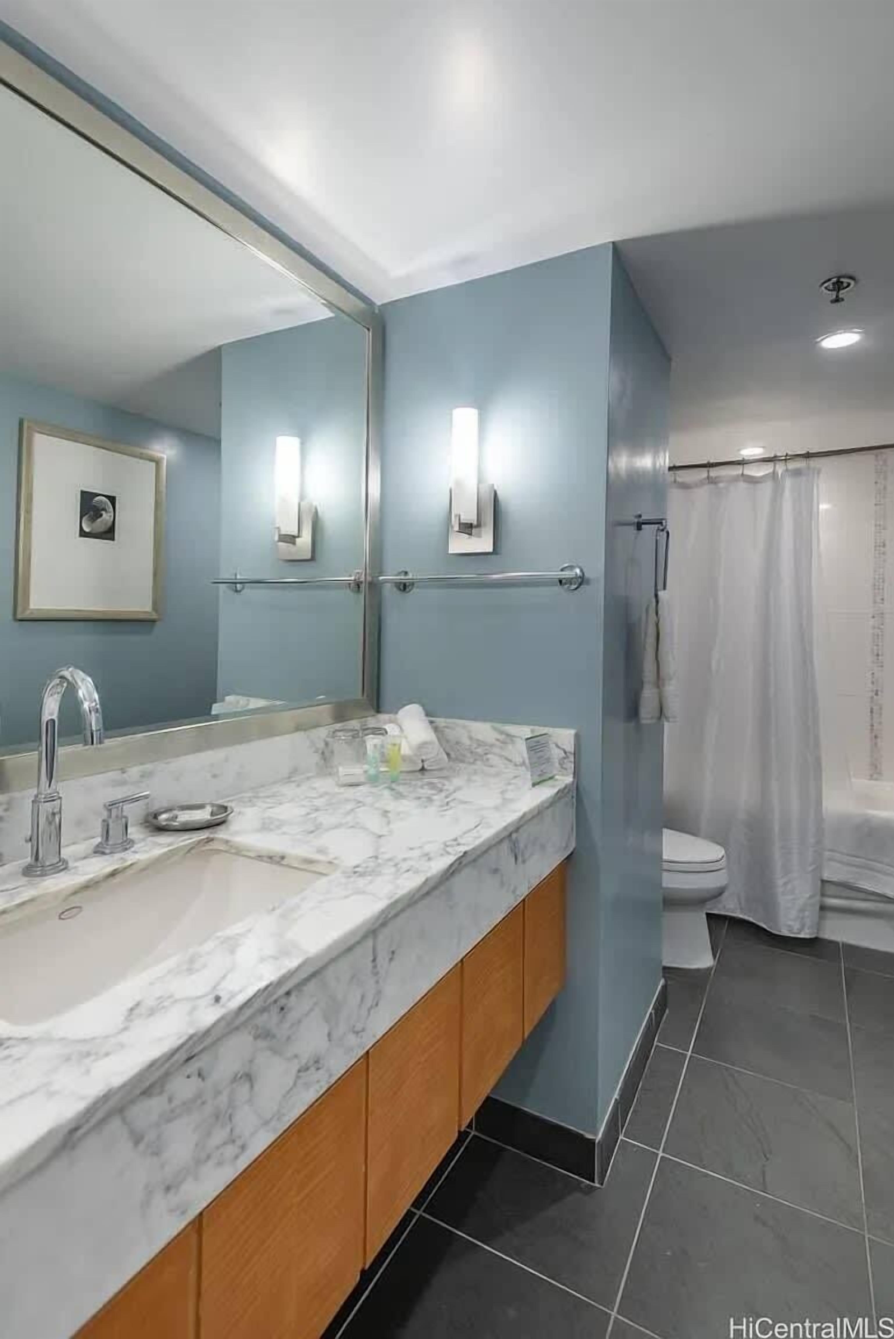 Un bany amb un lavabo de marbre, un mirall gran i un teló de dutxa.