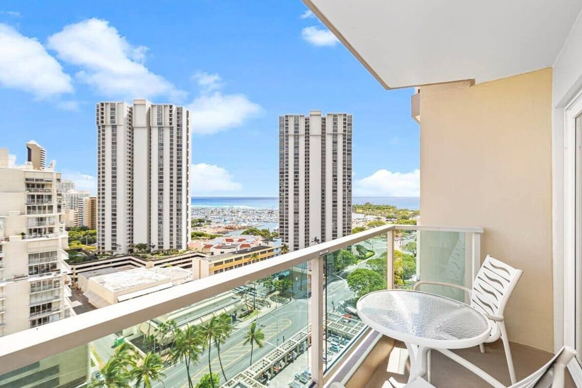 A balcony with a glass railing overlooking a cityscape with tall buildings and a clear sky.