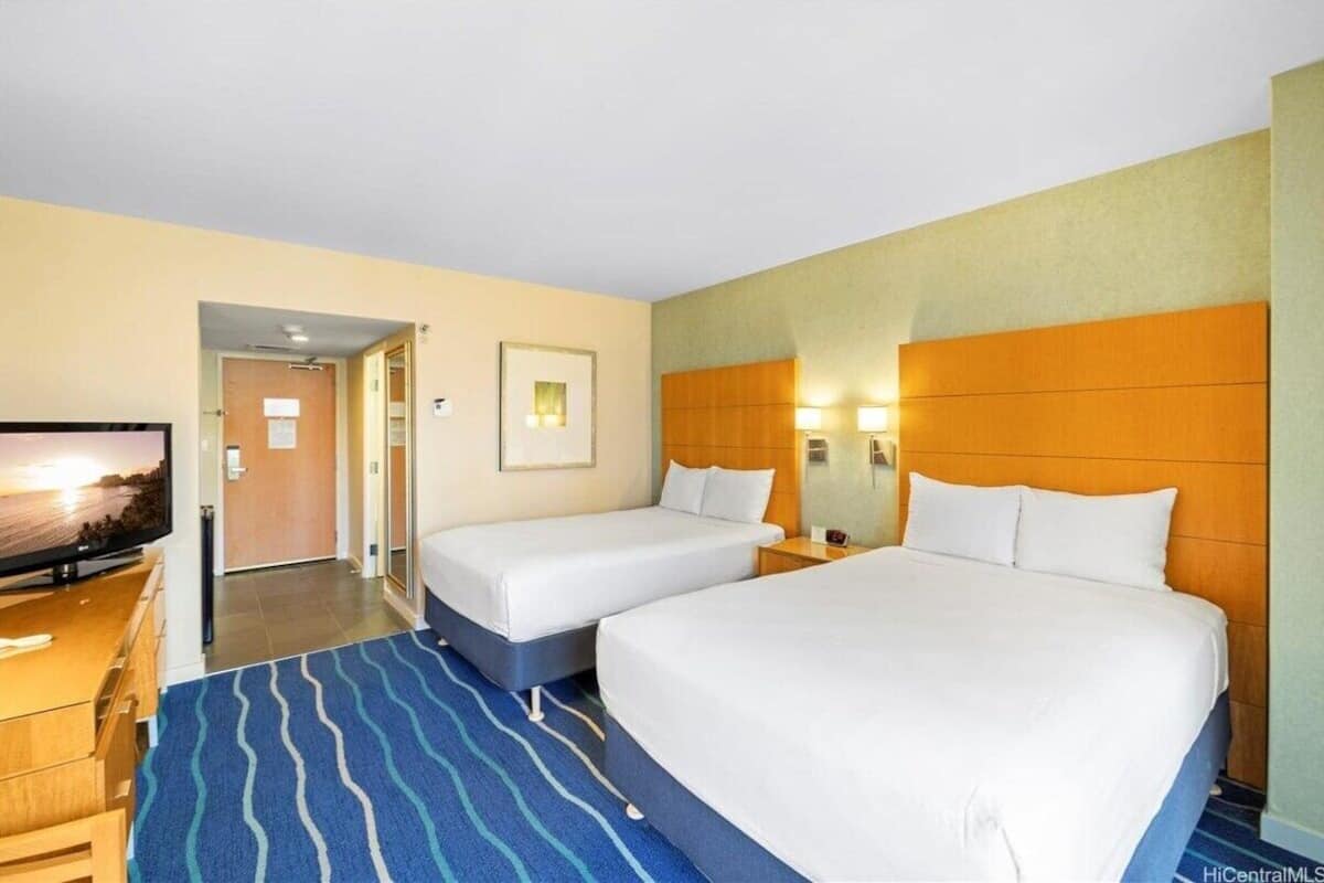 A hotel room with two beds, a television, a wooden headboard, and a blue striped carpet.