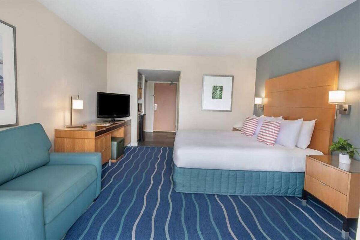 A hotel room with a bed, a TV, a desk, a chair, and a door leading to another room.
