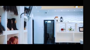 Un intérieur moderne avec des murs blancs, des étagères remplies de divers objets et une porte-fenêtre donnant sur une autre pièce.