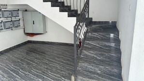 Un escalier avec une rampe en métal, un sol en marbre et des boîtiers électriques fixés au mur.