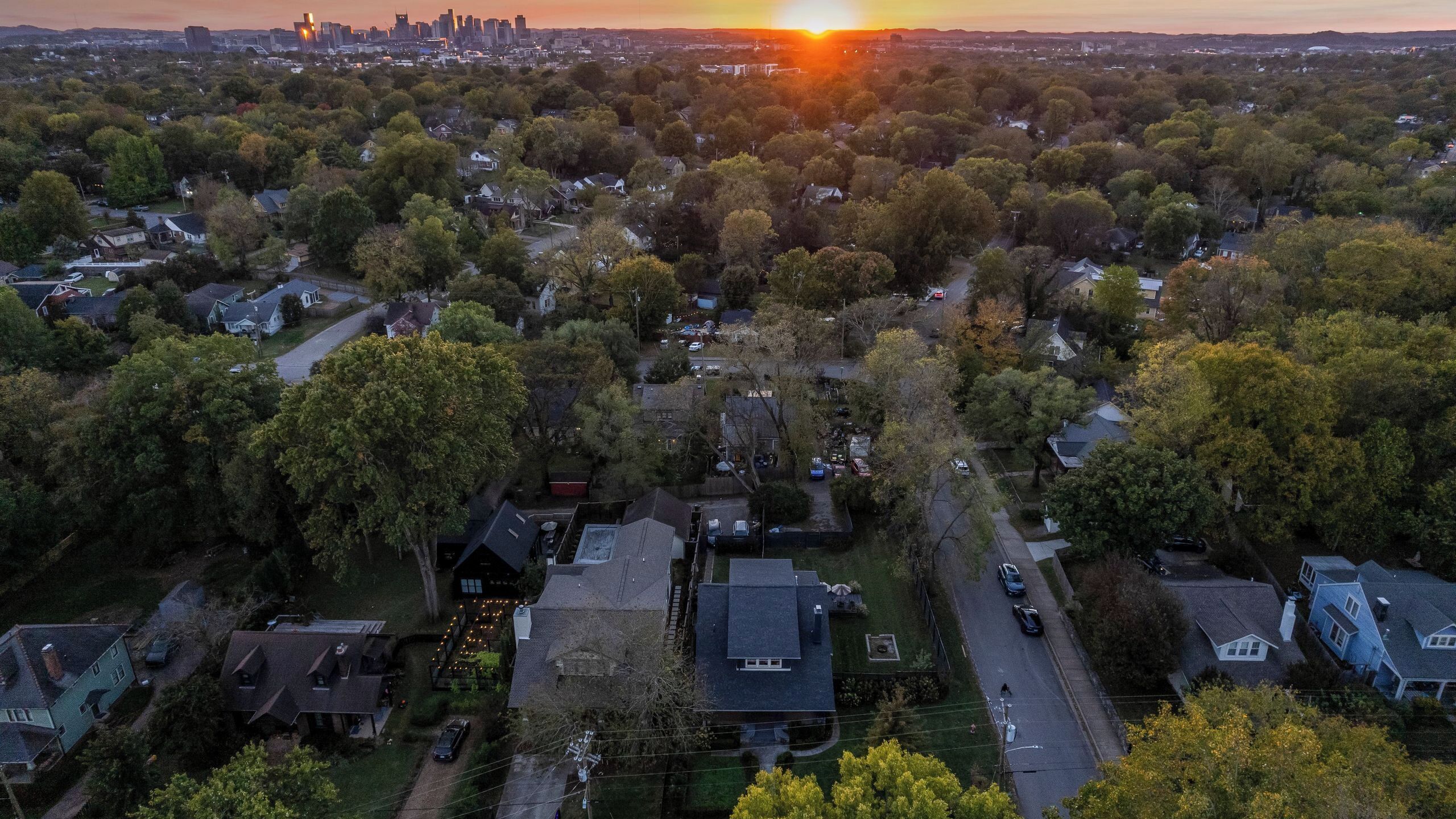 Une vue aérienne d’un quartier résidentiel, avec des maisons, des arbres et un coucher de soleil en arrière-plan.