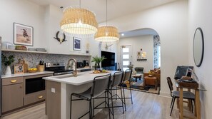 A modern kitchen with a central island, pendant lights, and a dining area with chairs and a table.