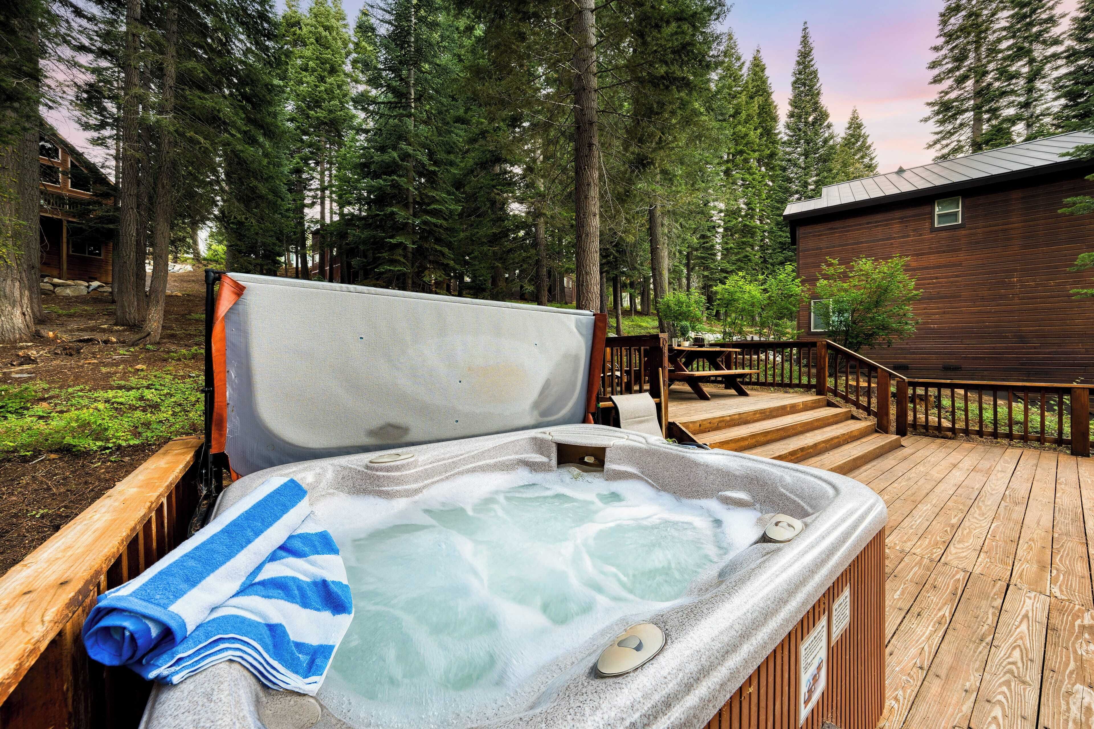 A hot tub with a blue towel, surrounded by a wooden deck and tall trees.
