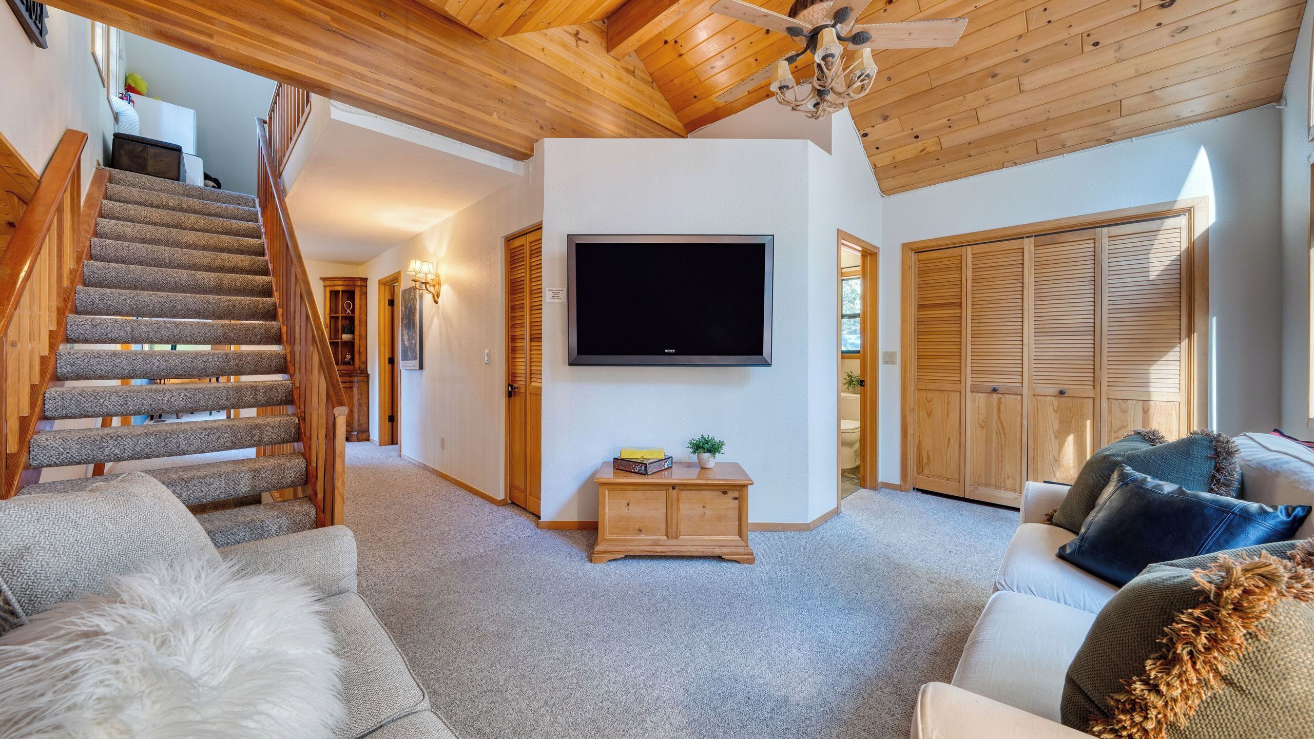 A spacious living area with a staircase, a flat-screen TV, wooden furniture, and a ceiling fan.
