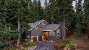 A two-story house with a dark exterior, a garage, and a driveway leading to a wooden deck. - Cozy Escape w/ Hot Tub + Deck & Access to Tahoe Donner & Skiing Alpenglow Chalet by Avantstay (Truckee)