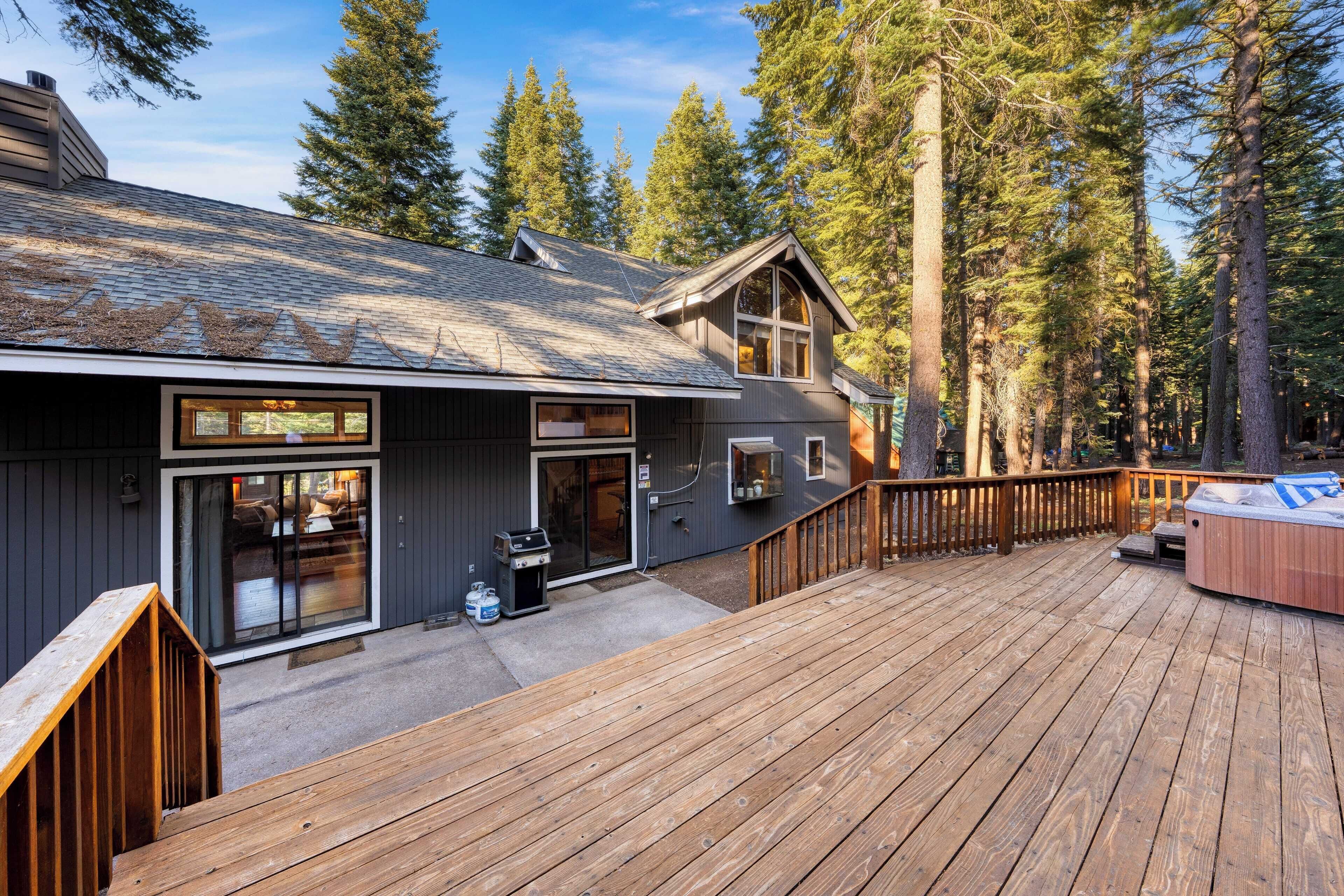 A cabin with a deck, a hot tub, and a sliding glass door leading to a patio area.
