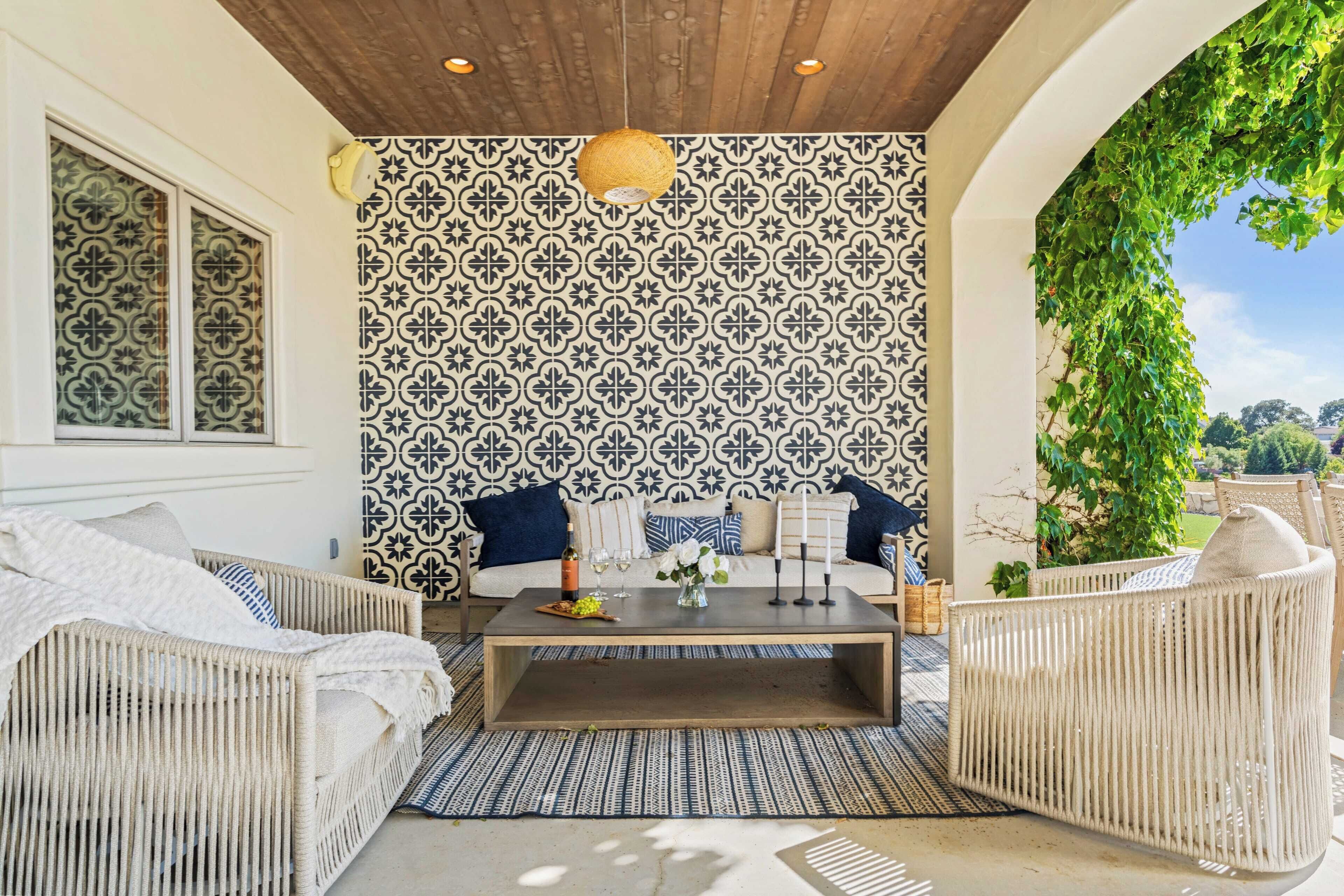A cozy outdoor seating area with wicker furniture, a patterned wall, and a hanging light fixture.