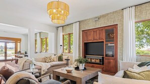 A spacious living room with a large wooden entertainment center, comfortable seating, and a large window offering a view of the outdoors. - Wine Country Escape w/ Views + Wine Cellar & Gym Caterina Dusi Vineyard by Avantstay (Paso Robles)