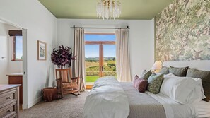 Une chambre à coucher avec un lit, une chaise, une vue sur la campagne et un lustre.