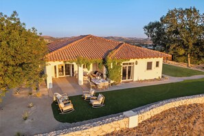 A house with a tiled roof, a patio with outdoor furniture, and a well-maintained lawn. - Wine Country Escape w/ Views + Wine Cellar & Gym Caterina Dusi Vineyard by Avantstay (Paso Robles)